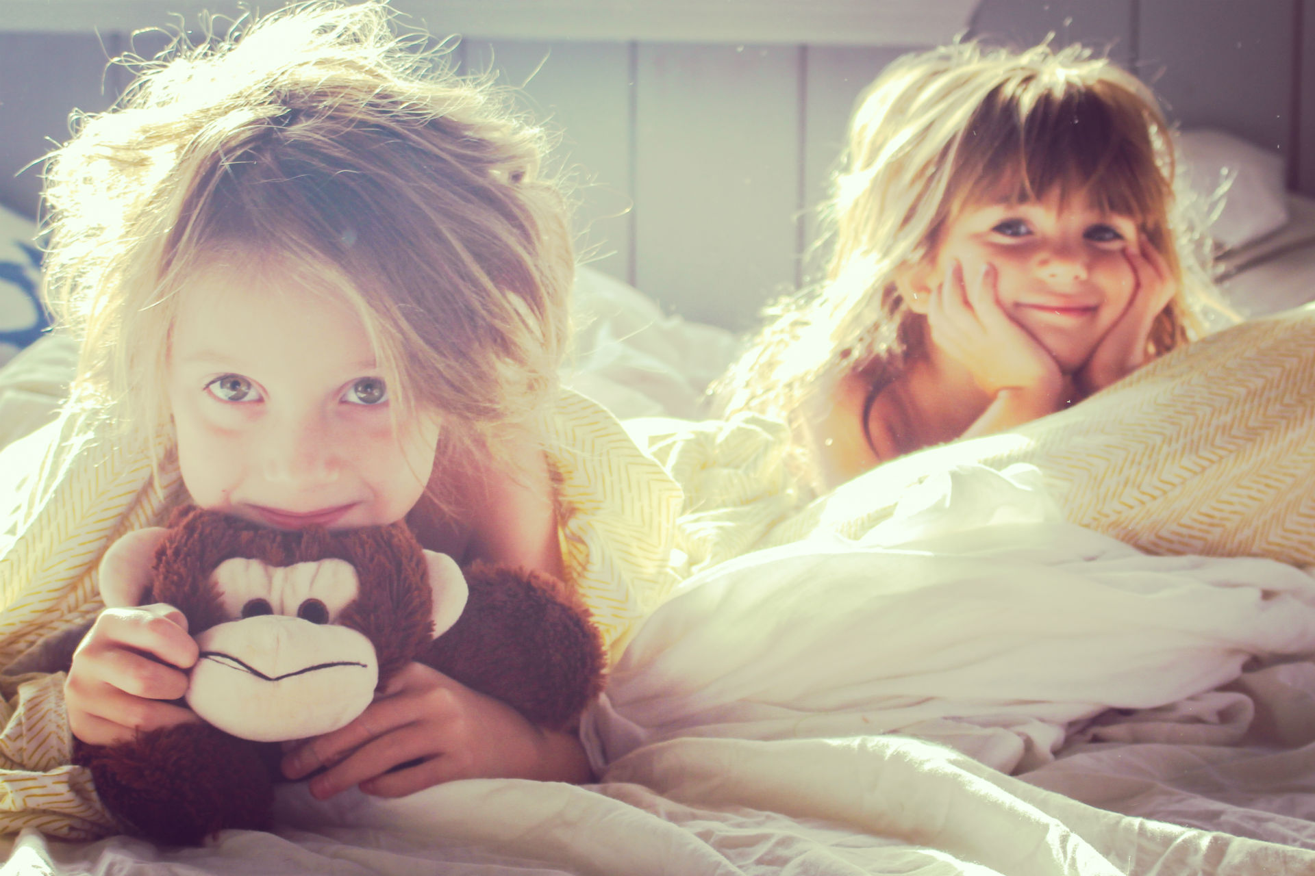two girls laying in bed, one holding a stuffed monkey
