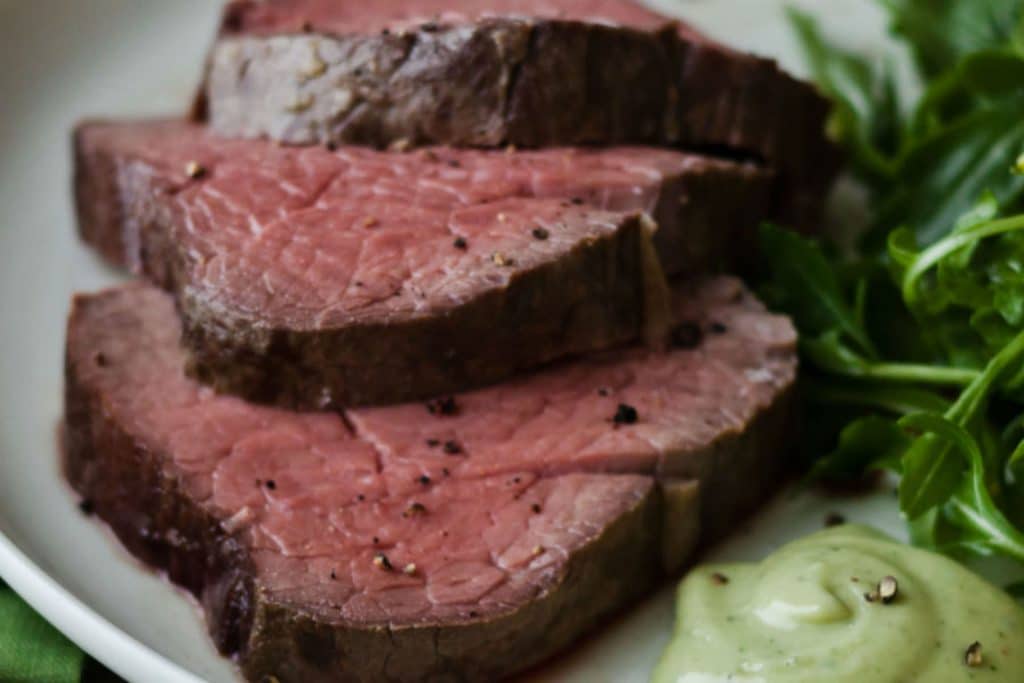 medium-rare beef sliced on a plate with a side salad