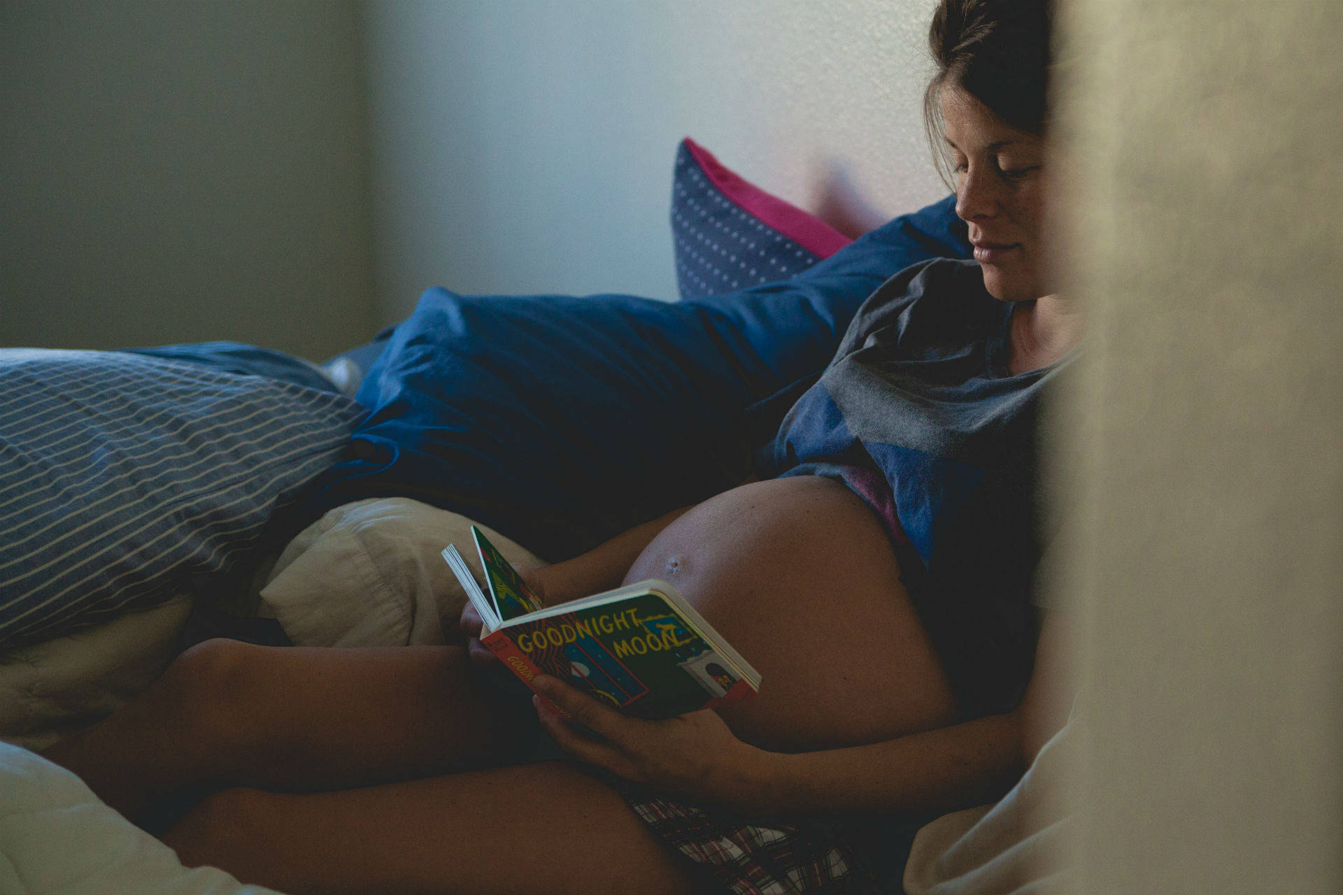 pregnant woman sitting in bed reading Goodnight Moon to her bump