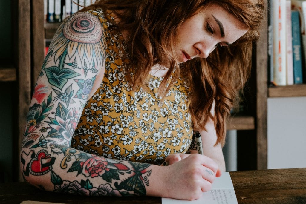 woman with tattoo at a desk writing