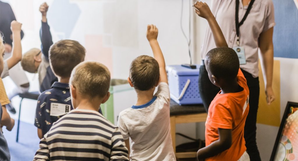 children in a classroom with their hands raised