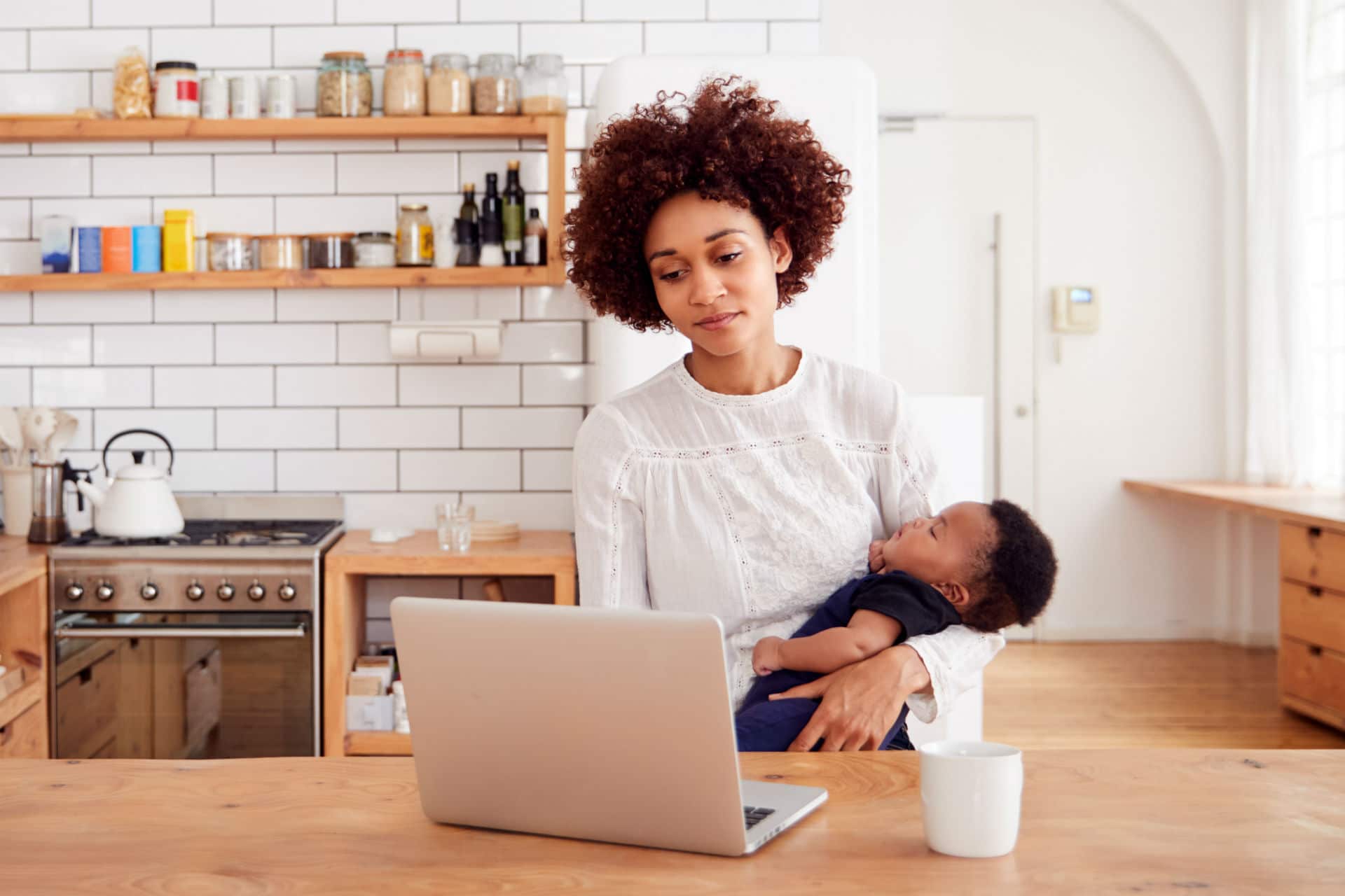 mother holding a baby while at a laptop