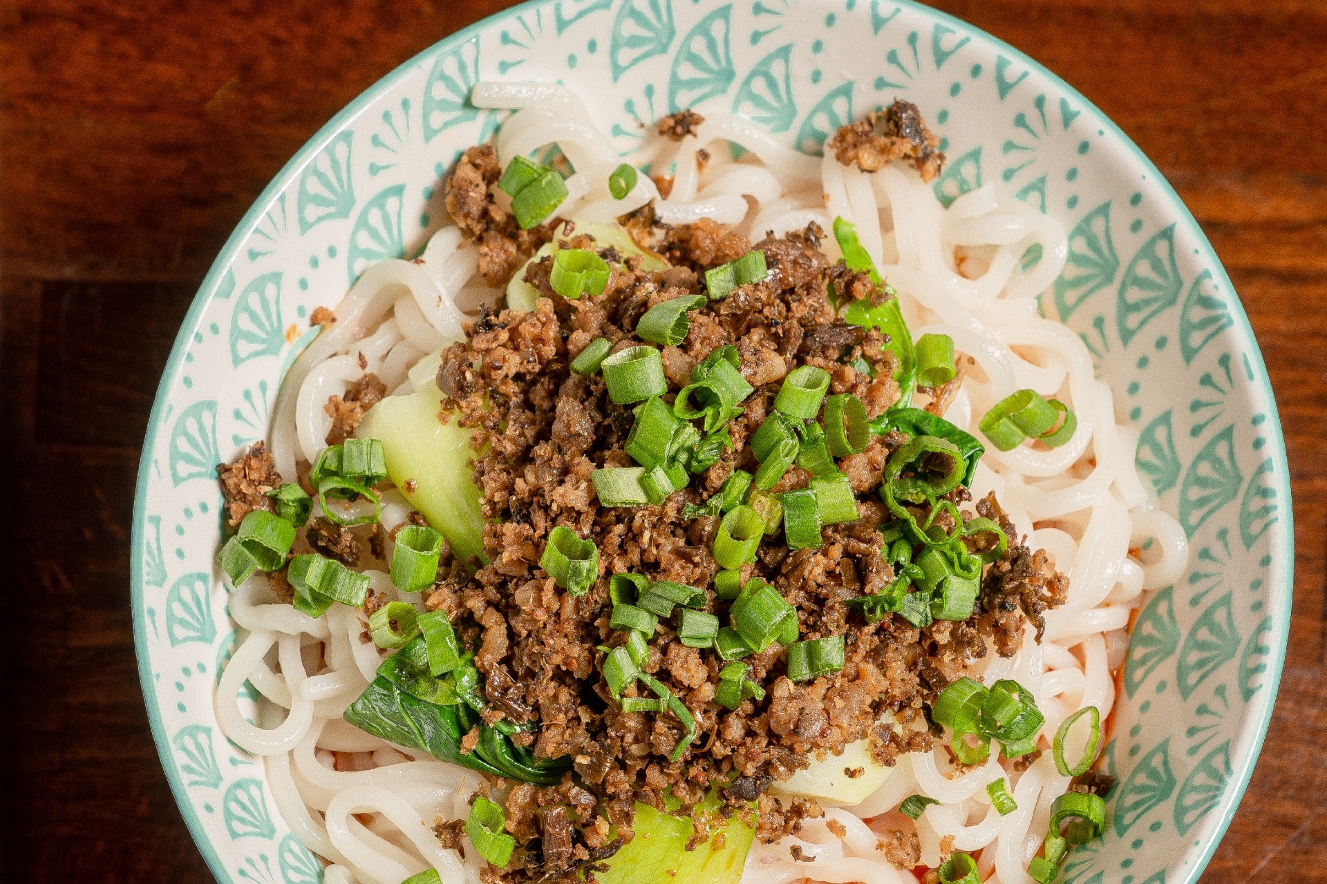 plate of noodles topped with ground pork and green onions in a dandan noodle dish
