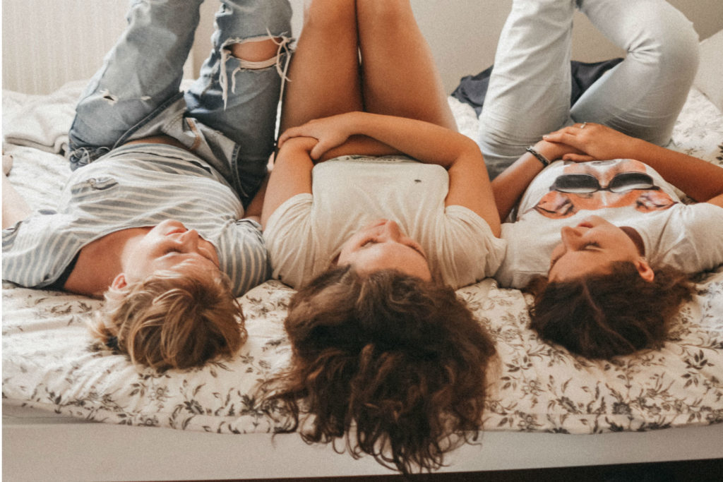 three teen girls laying upside-down on bed