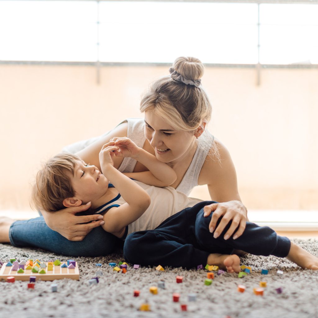 White mom and son sitting on floor together playing with multi-coloured blocks. How To Support Mothers Raising Children With Autism