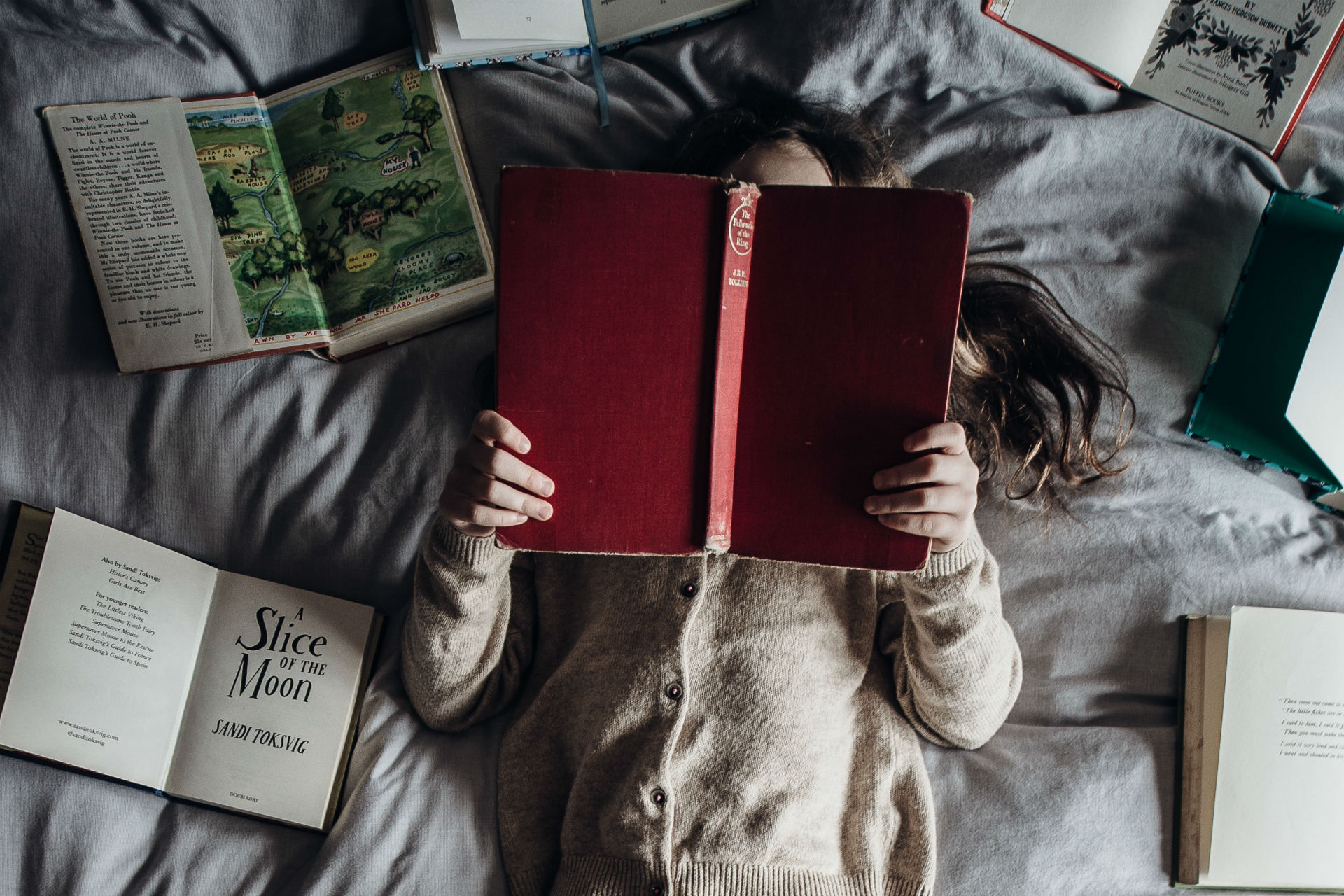 child reading in bed surrounded by books