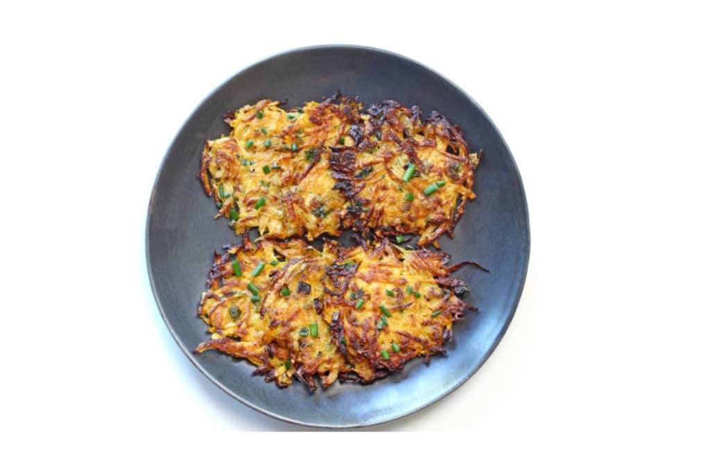 two squash latkes on a black plate flecked with green onion