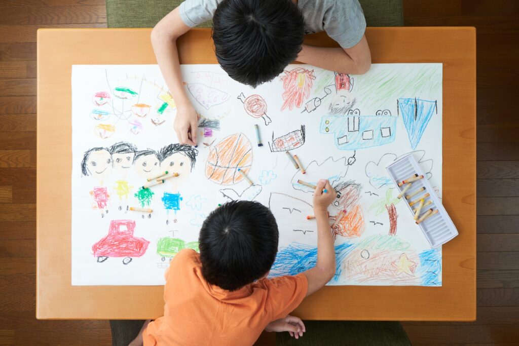 two friends are colouring a large piece of paper together. Image is shot from overhead