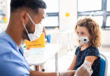 4 ways to help kids cope with needles a nurse in a mask prepares a girl in a mask for a needle
