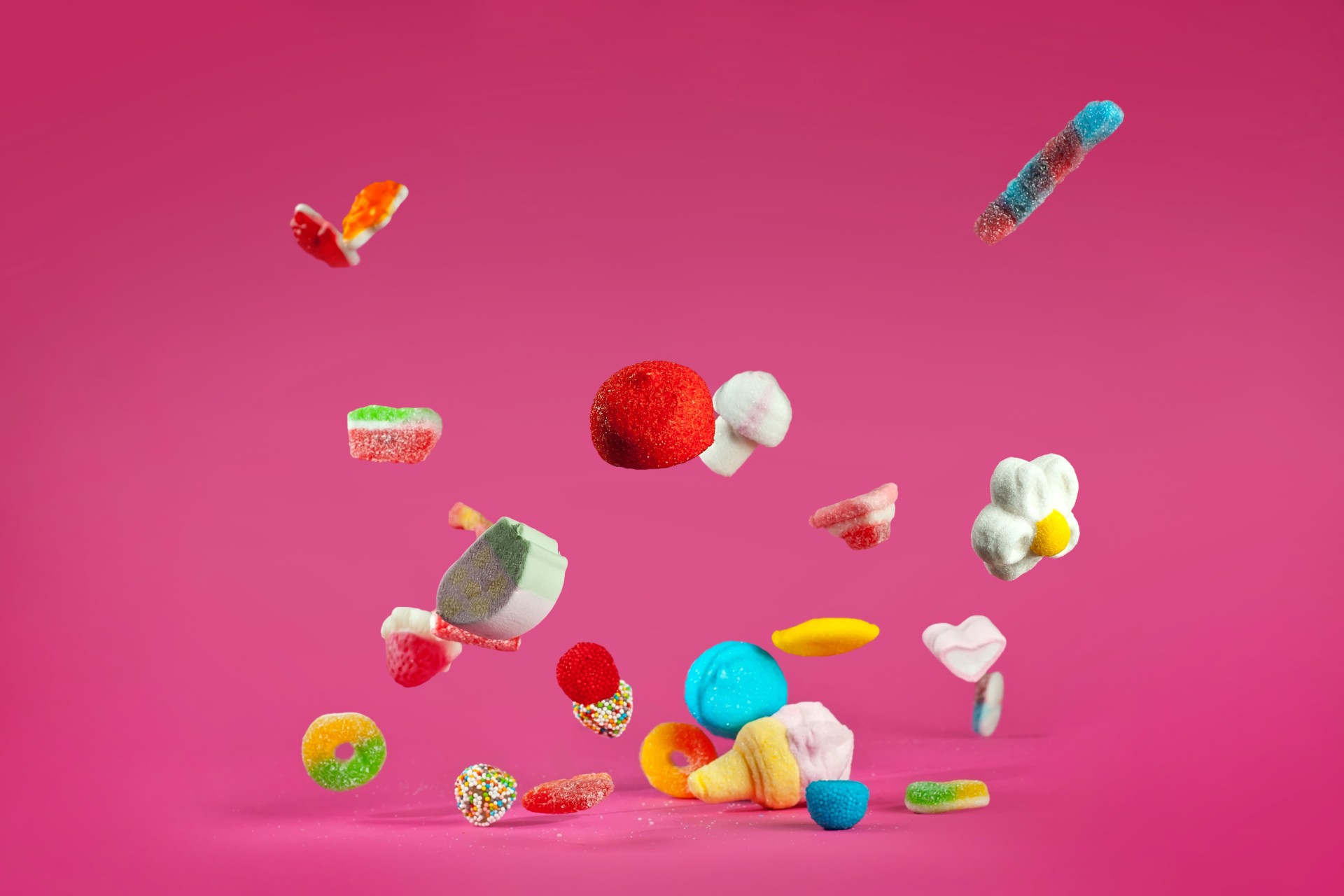 a pile of gummy, sugar-filled candy falls in front of a bright pink background