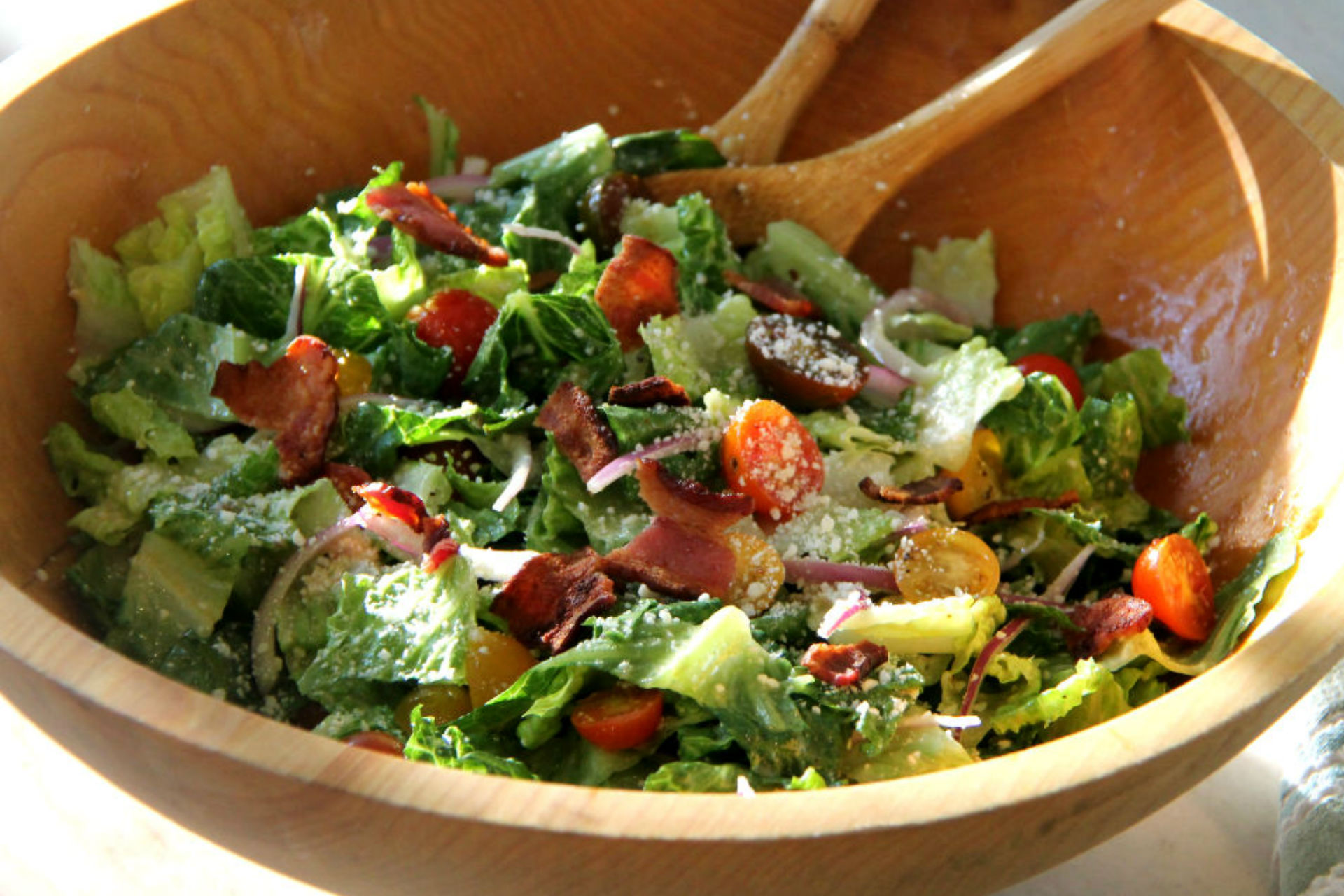 wooden bowl with caesar salad, tomatoes and bacon