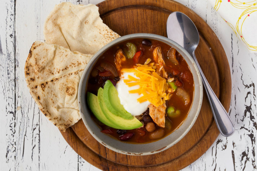 bowl of chili with sour cream, cheese and avocado