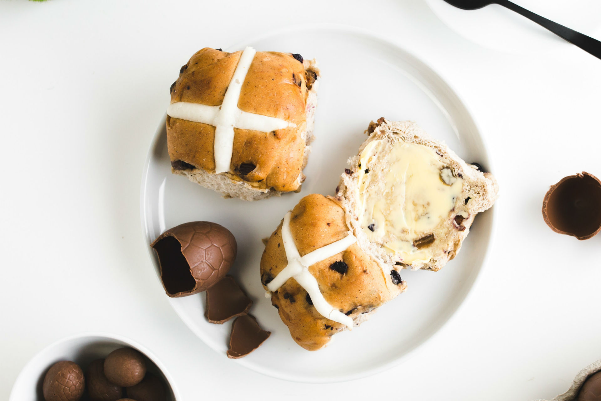hot cross buns on a plate with chocolate eggs