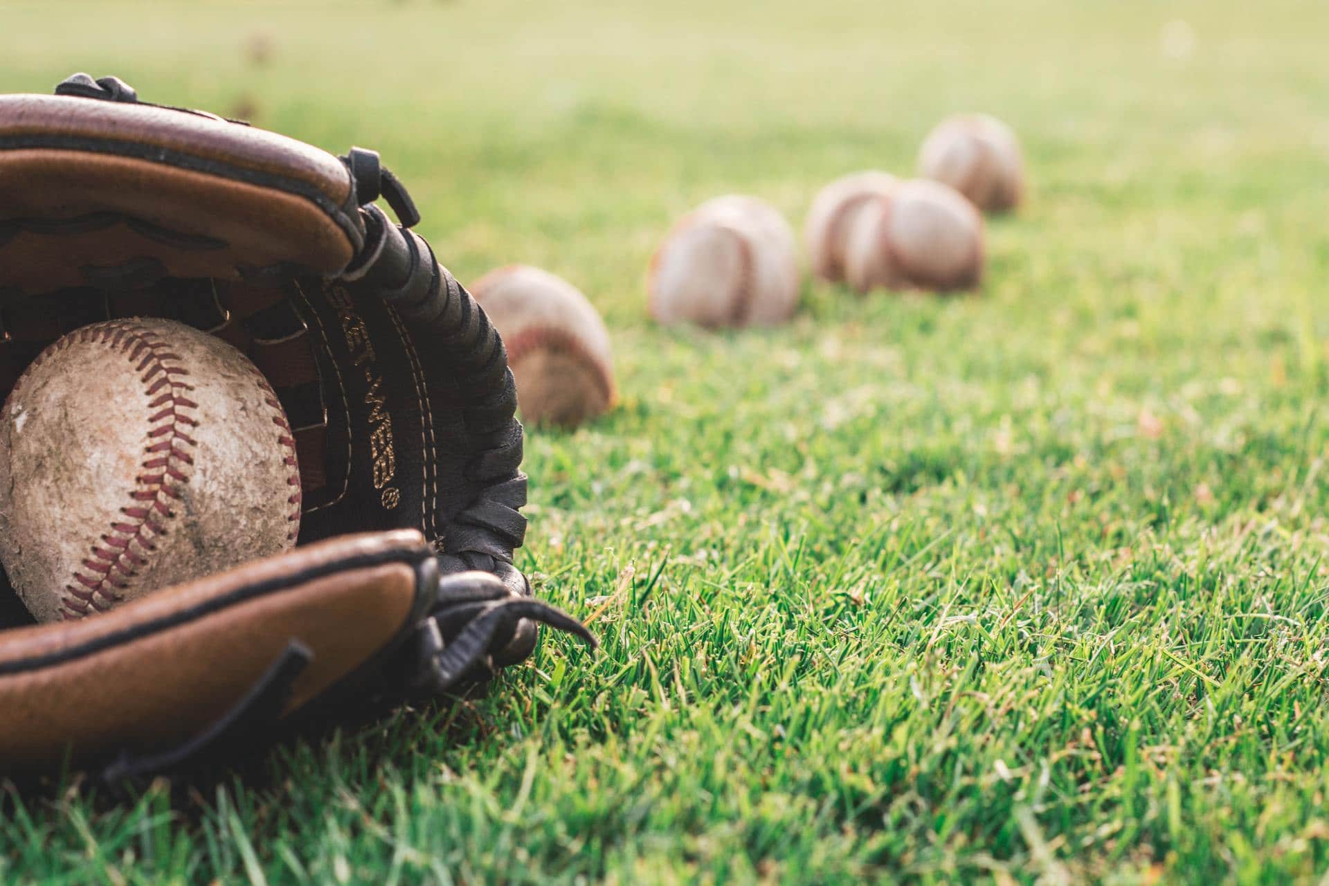 Baseball glove and baseballs lying in the grass