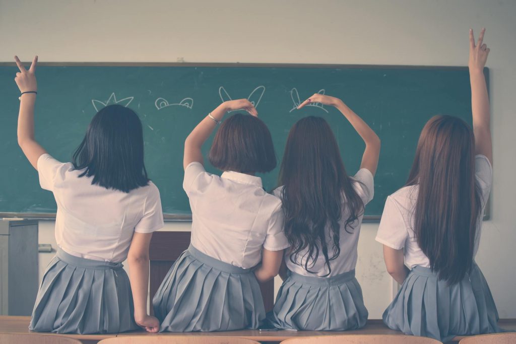 Four girls in school uniforms making funny hand signals