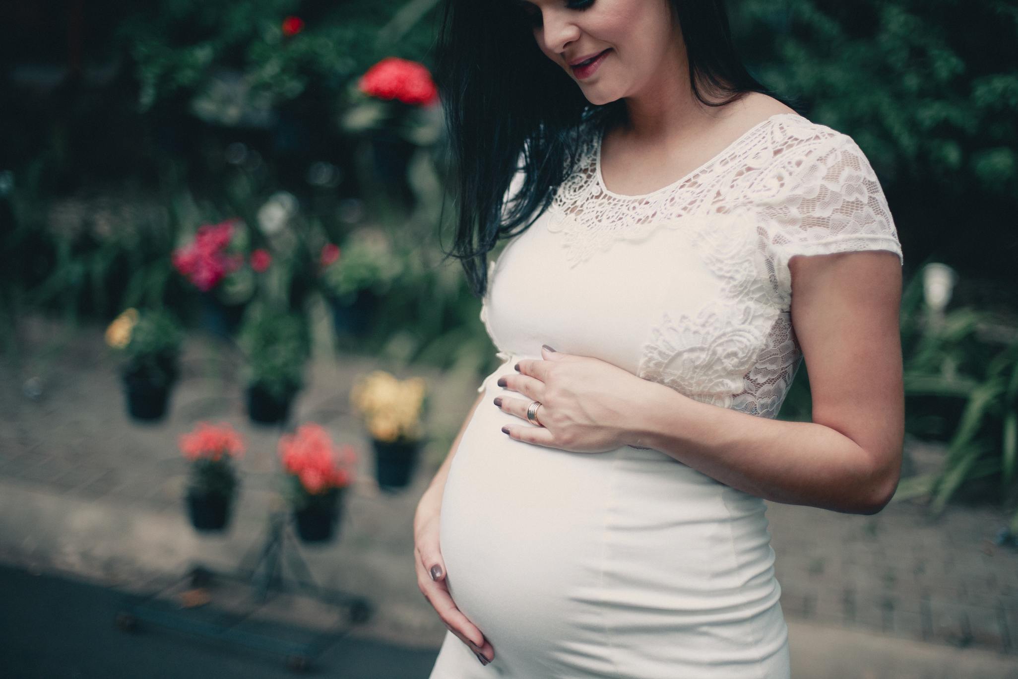 Pregnant woman in white lace dress looking down