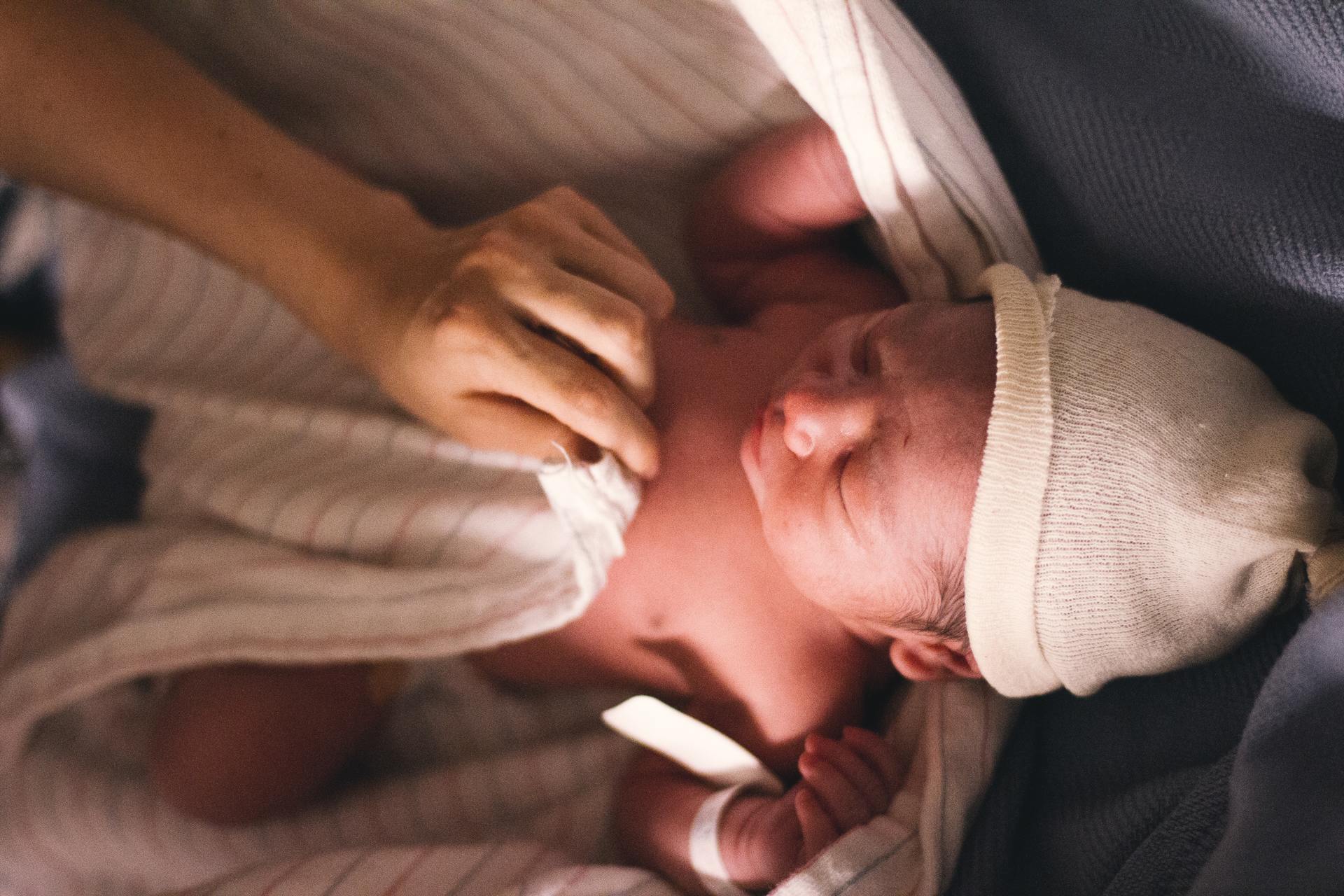 Newborn baby in hat being wrapped in a blanket