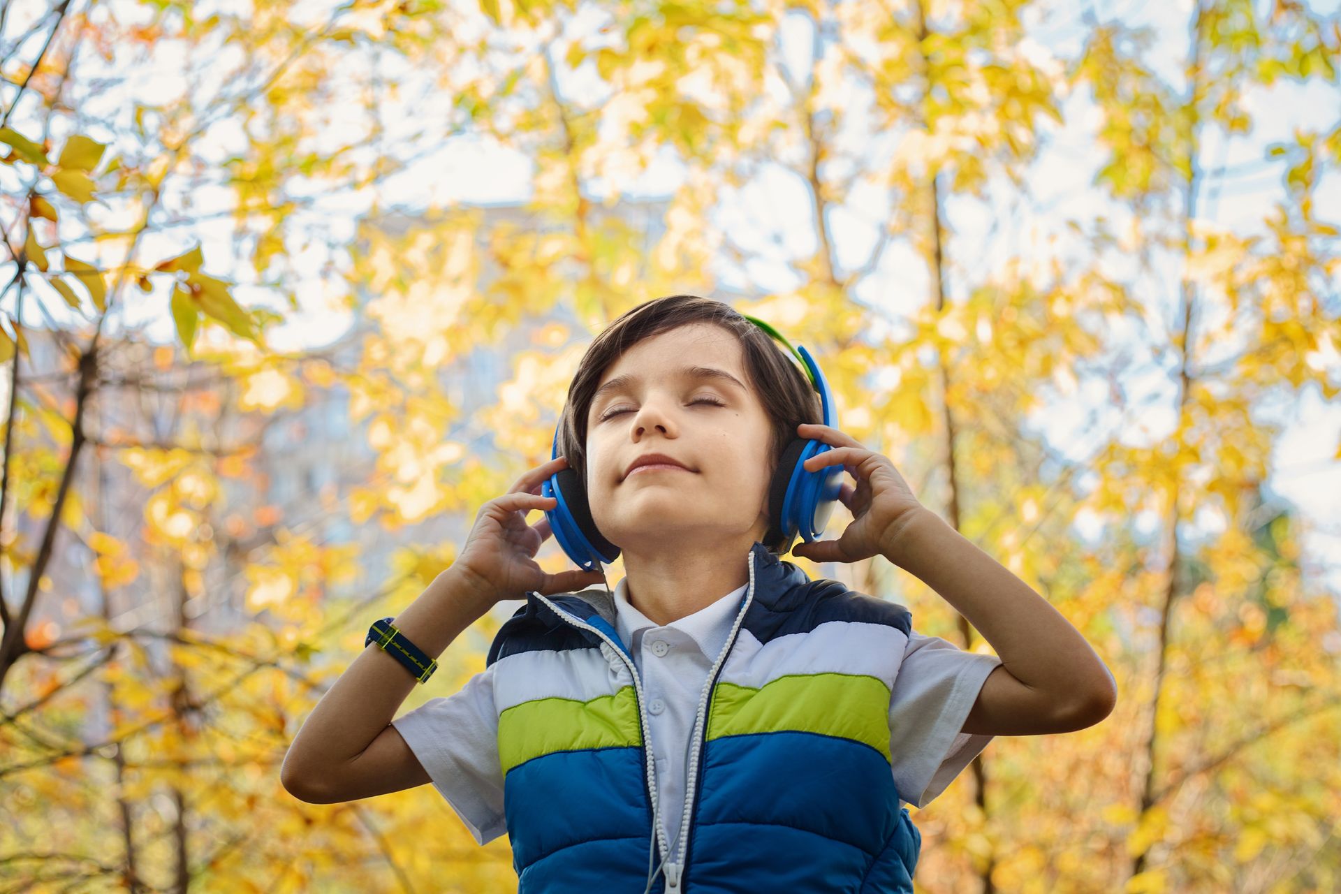 Young boy in striped vest listening to blue headphones