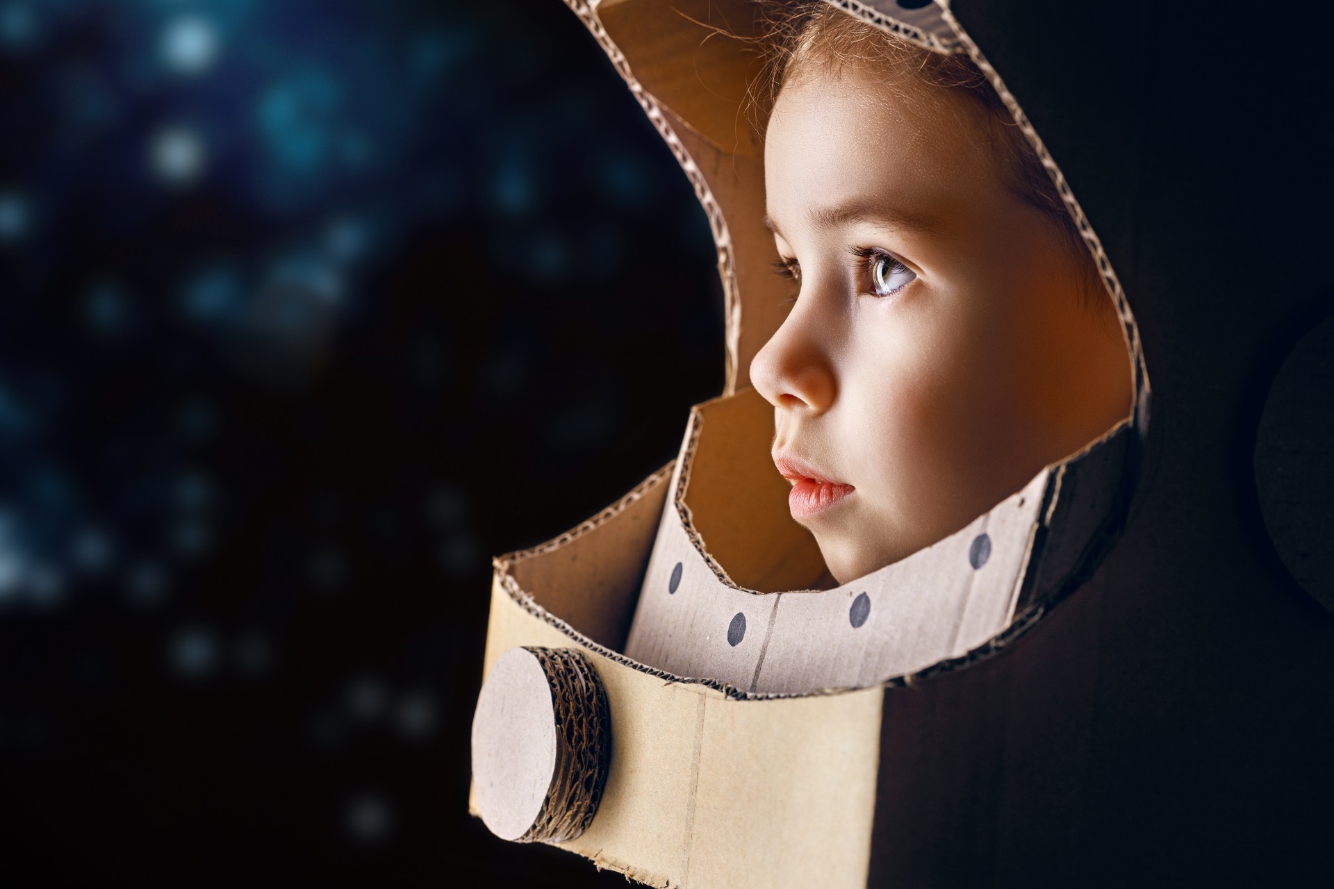 a child plays pretend wearing a space helmet made of cardboard