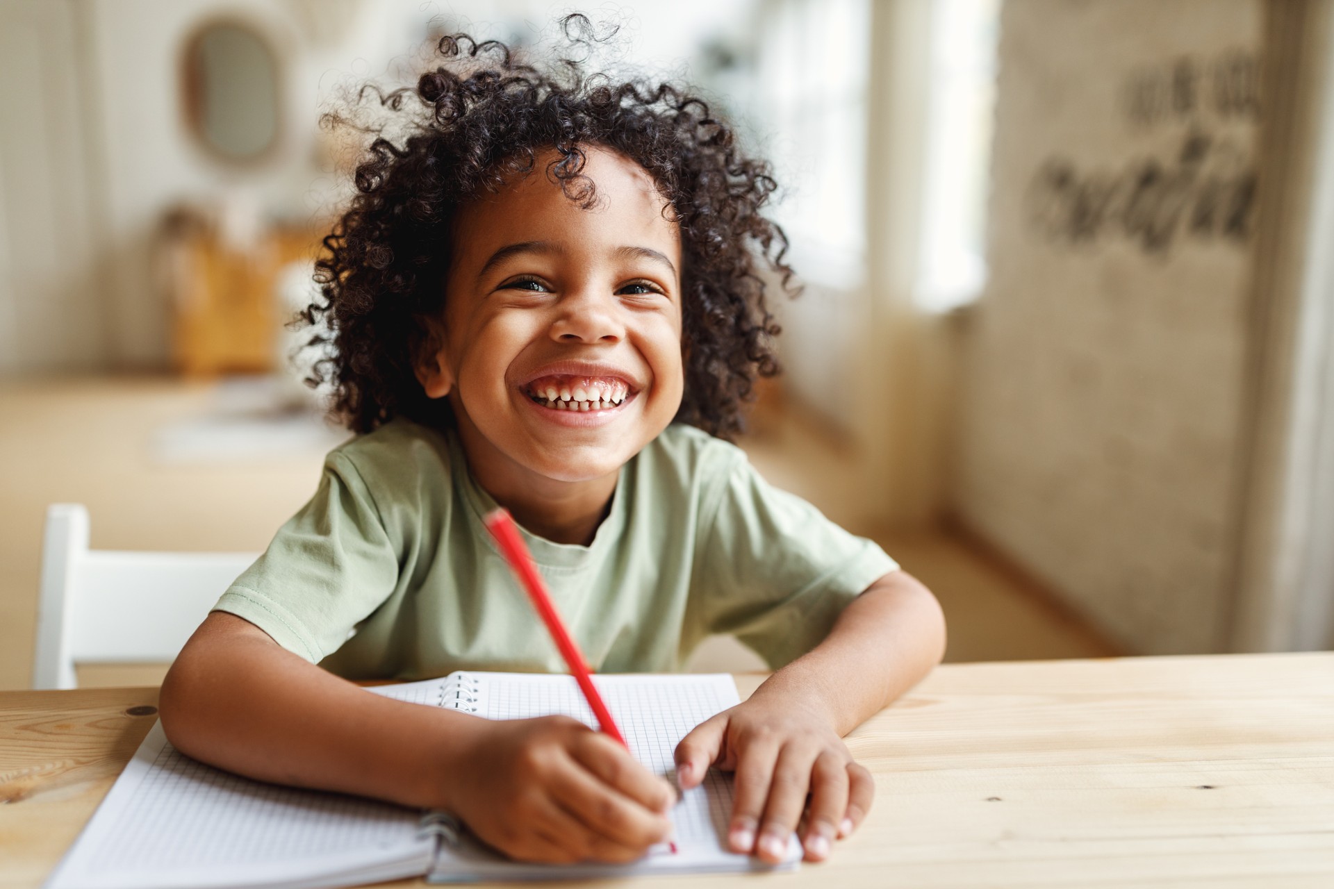 Child with a pen and paper looking happy to practice writing