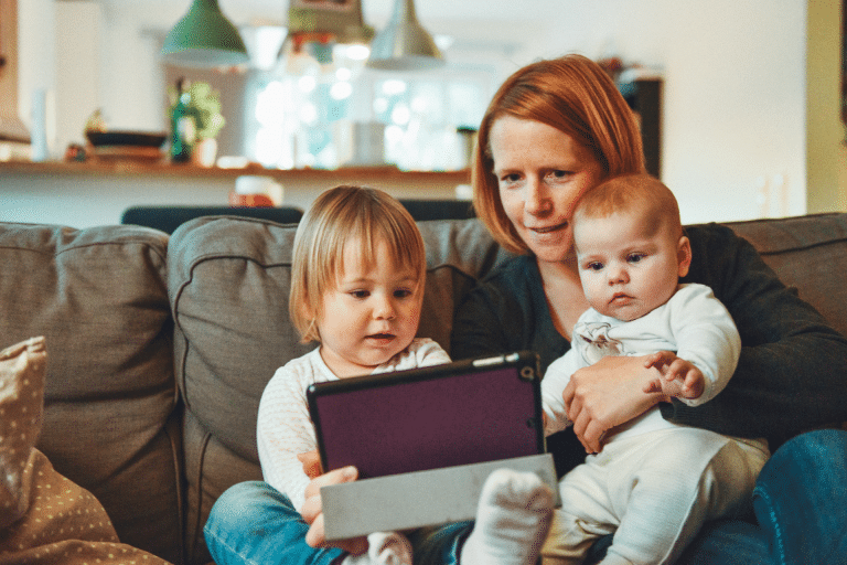 mother holding two kids and looking at a tablet with them