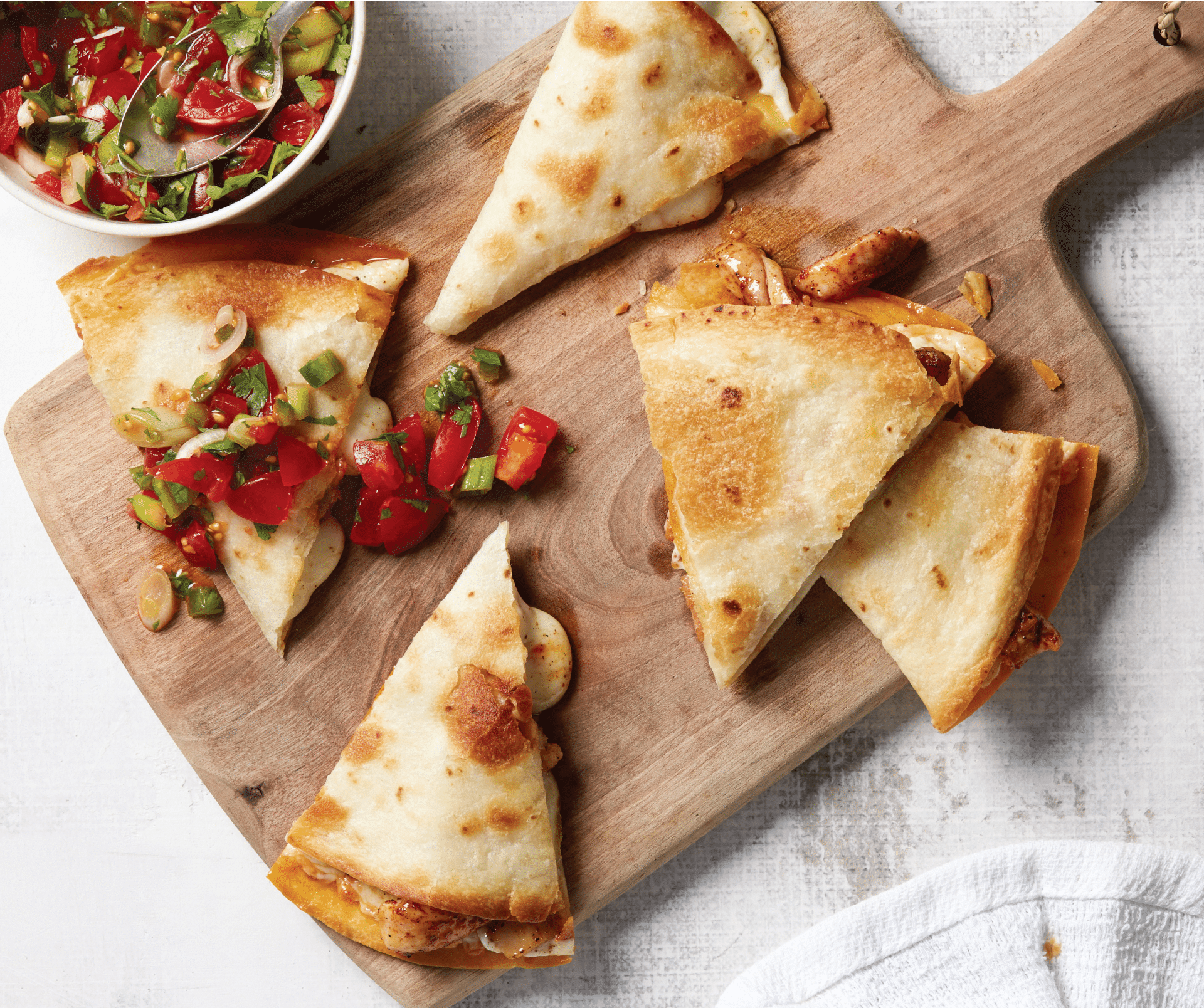 Chicken quesadillas on a wooden cutting board with salsa on the side