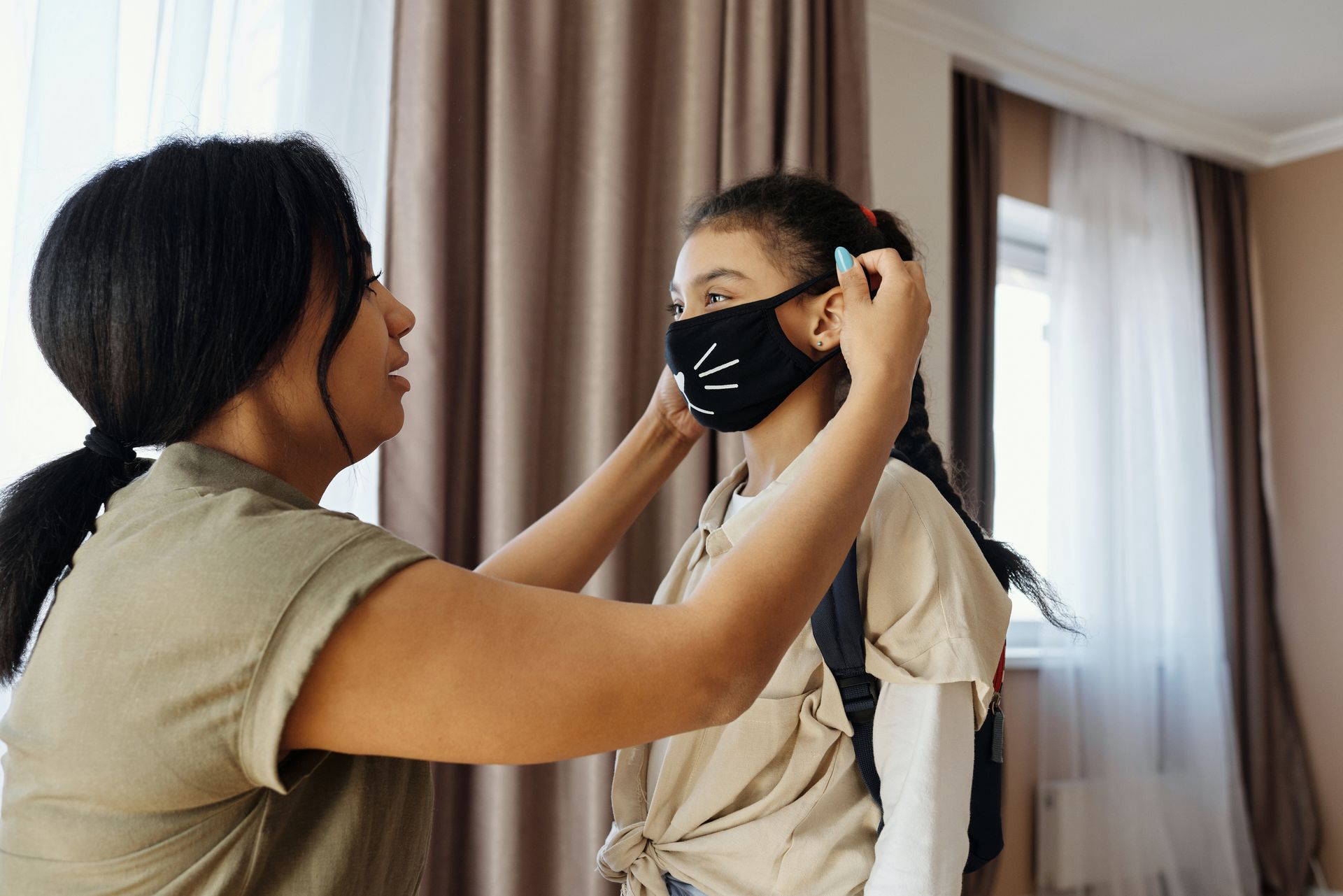 Woman with dark hair helping a child put on a mask