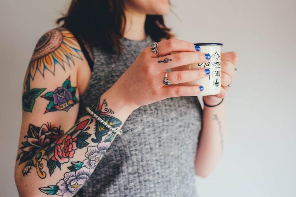 woman with tattoos on her arm holds a cup of coffee to her chest