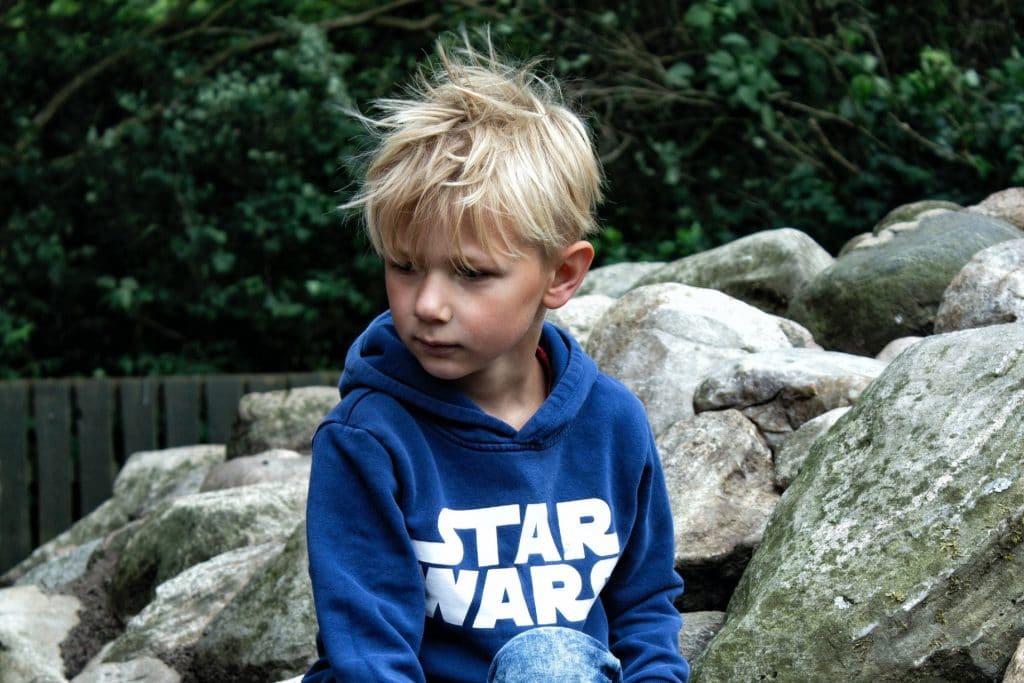 boy with blonde hair looks away from camera and appears sad