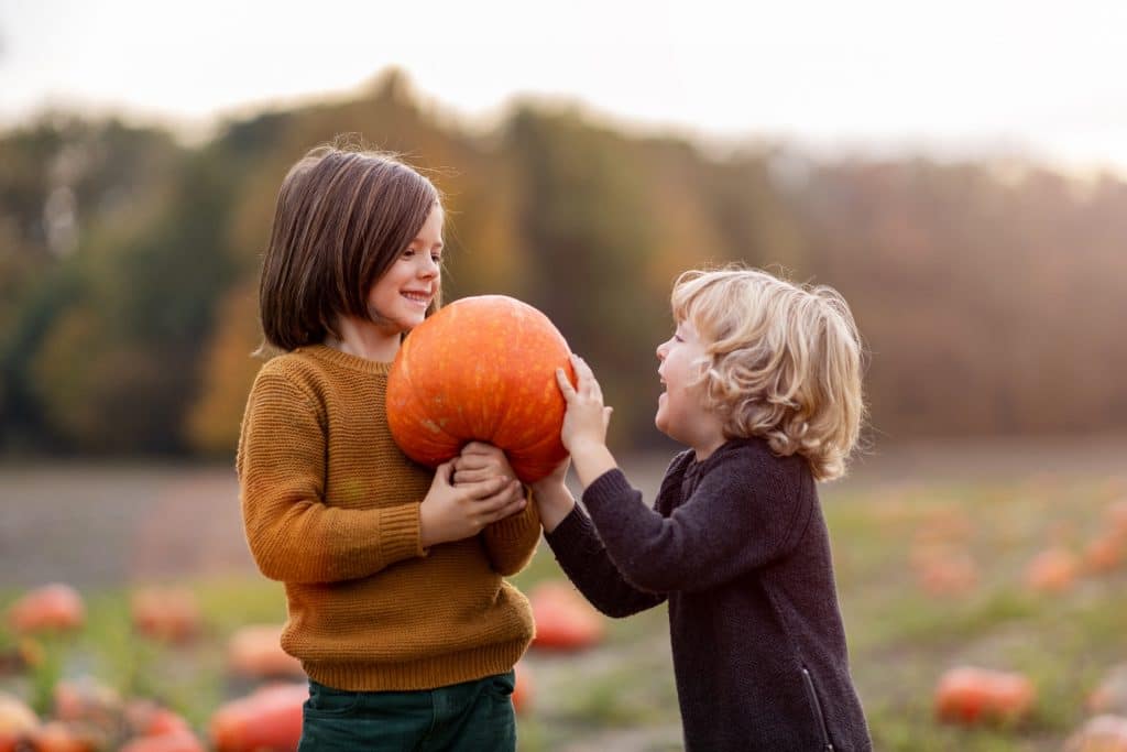 two kids holding a pumpkin in a pumpkin patch