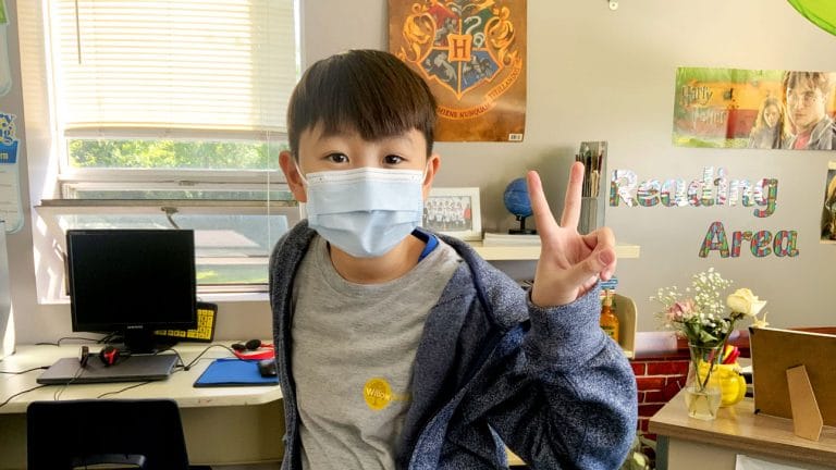 boy wearing mask at school and giving the peace sign