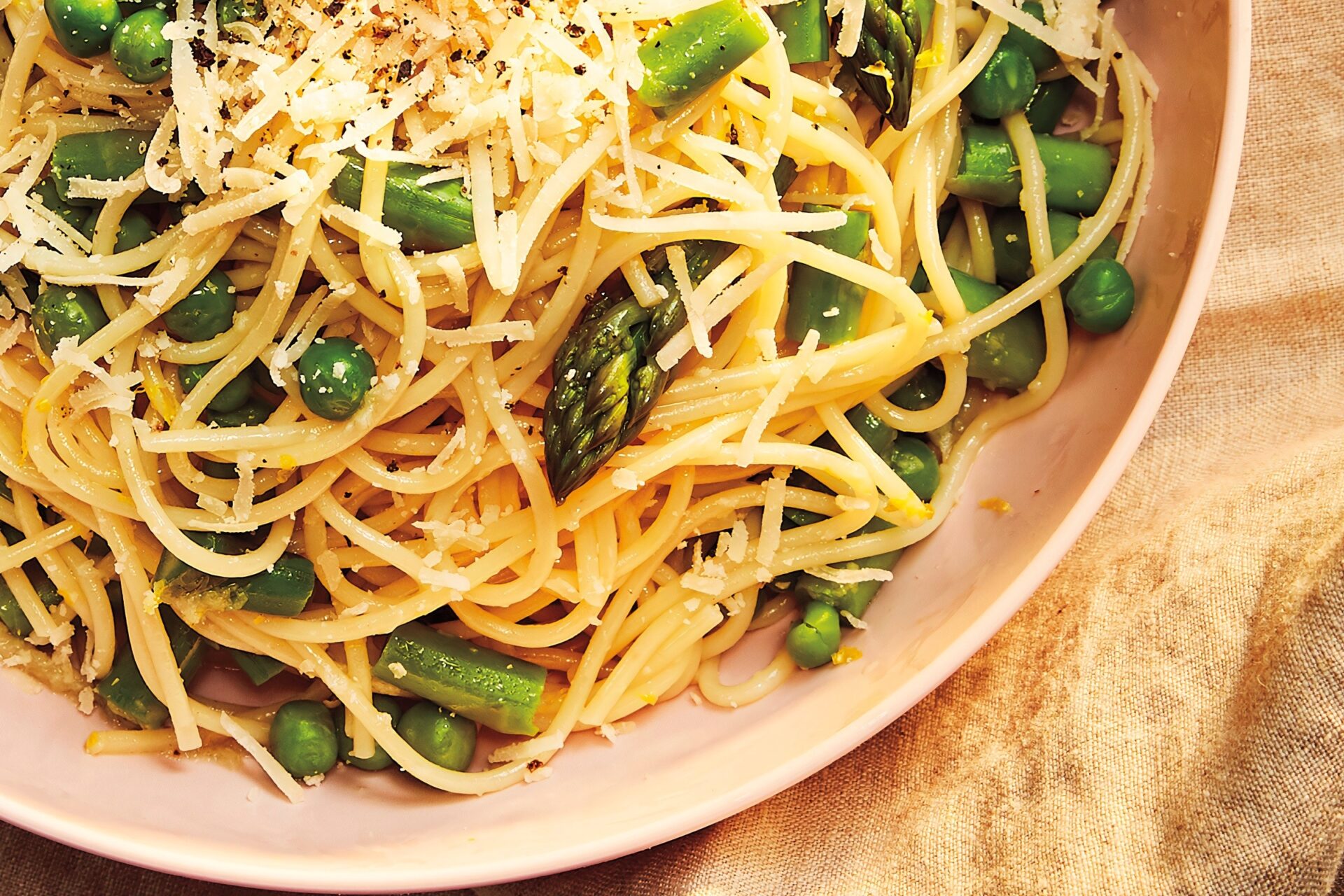 plate of spaghetti noodles with cheese, lemon, peas and asparagus