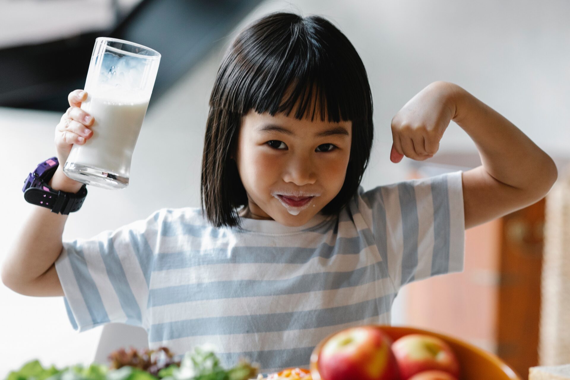 Little girl flexing muscles while drinking a glass of milk