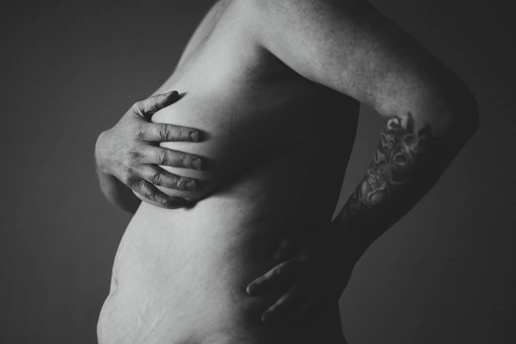 black and white photo of a woman with a normal stomach and stretch marks holding her breasts