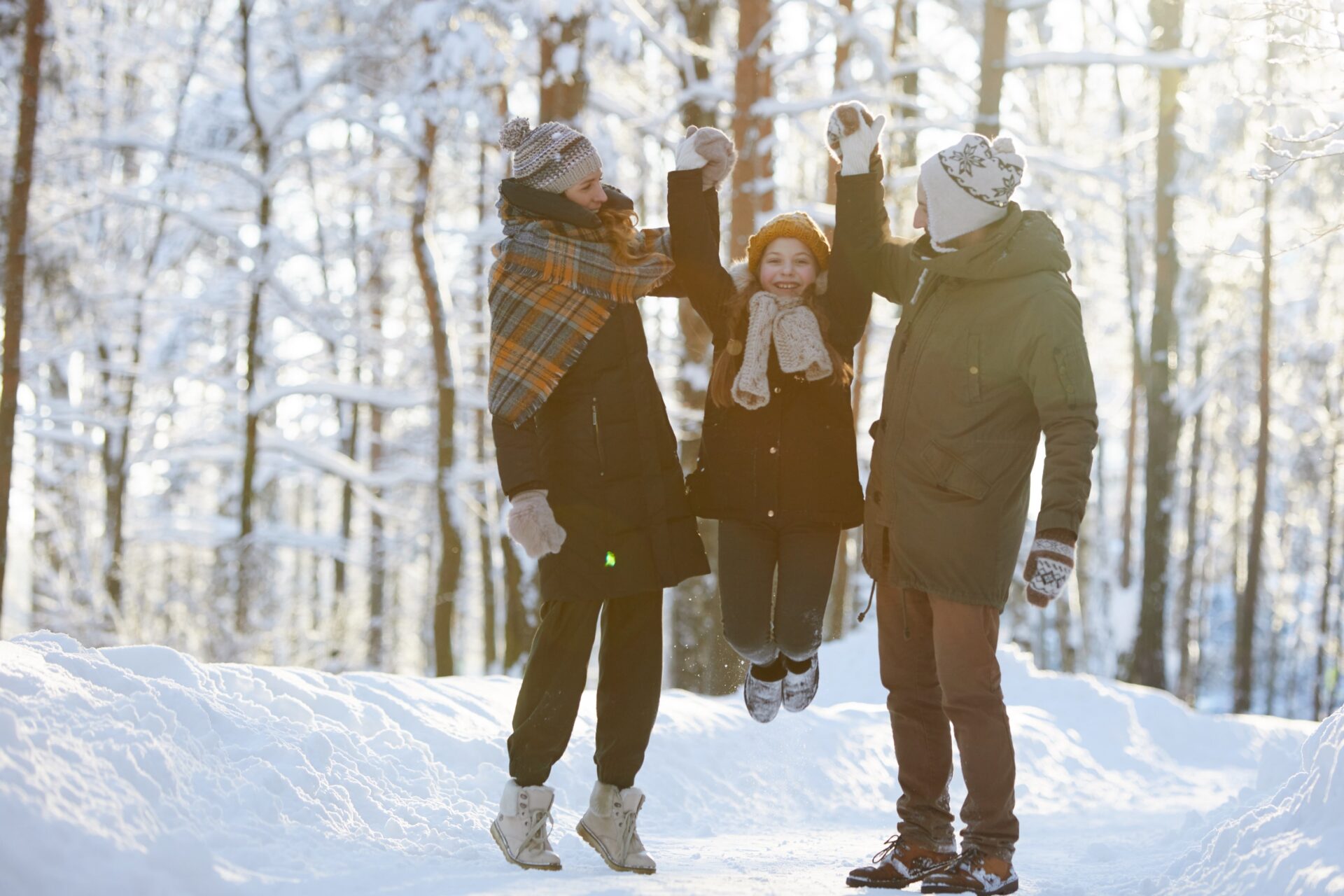 a family walks in the winter looking happy, the daughter is being lifted by her parents on both sides