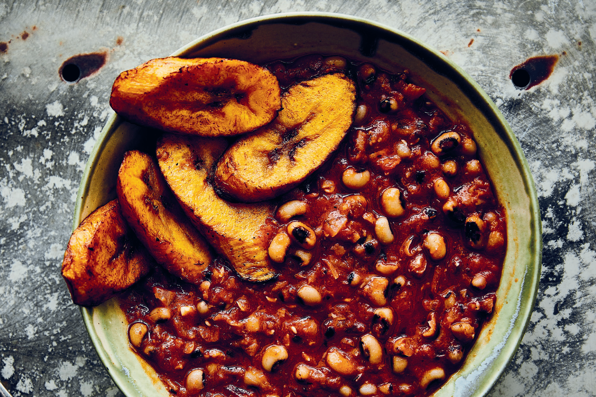 bowl of stewed beans in a sauce with fried plantains
