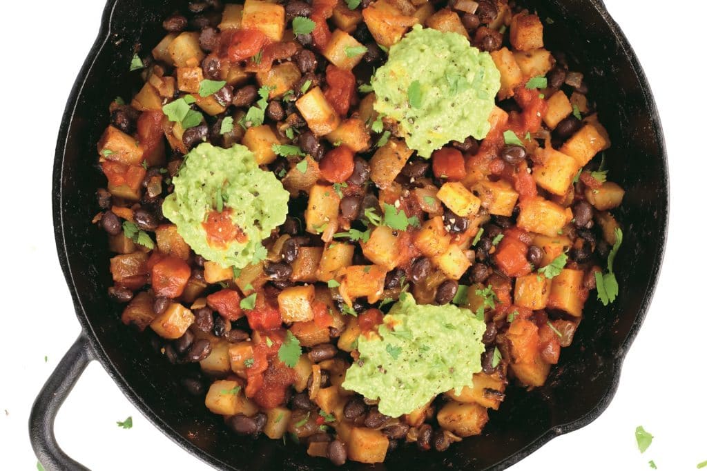 Skillet with potato and black bean hash and scoops of guacamole