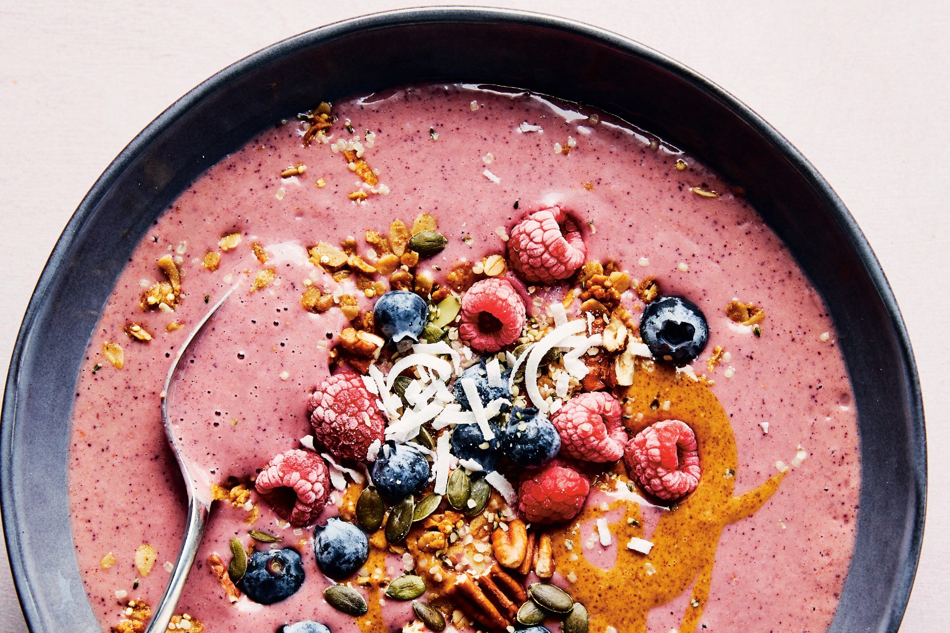 pink smoothie bowl with fresh berries, oatmeal and nut butter on top