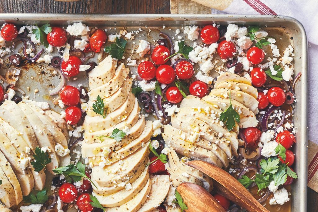 warm greek chicken salad recipe: sheet pan with chicken, tomatoes and olives