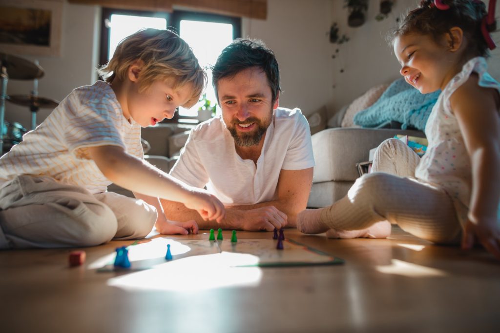 Father and two kids sit on the floor playing a boardgame