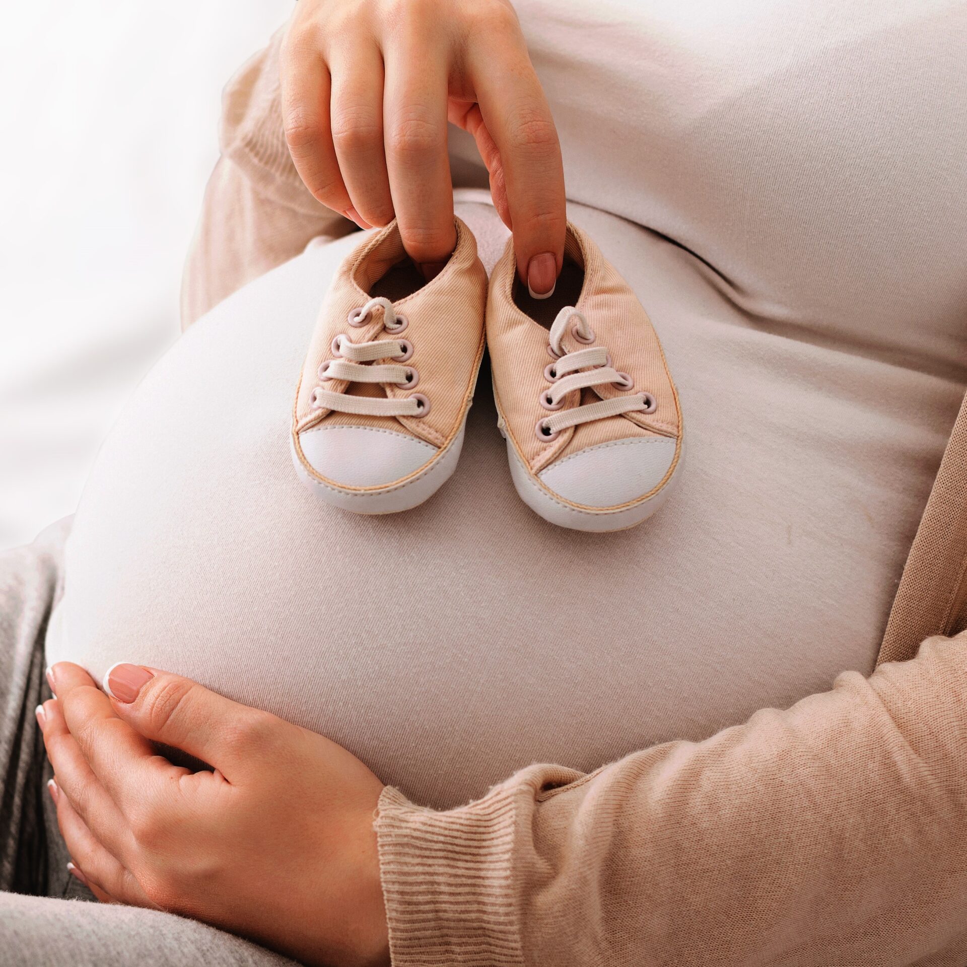 Mom holding baby shoes on pregnant tummy
