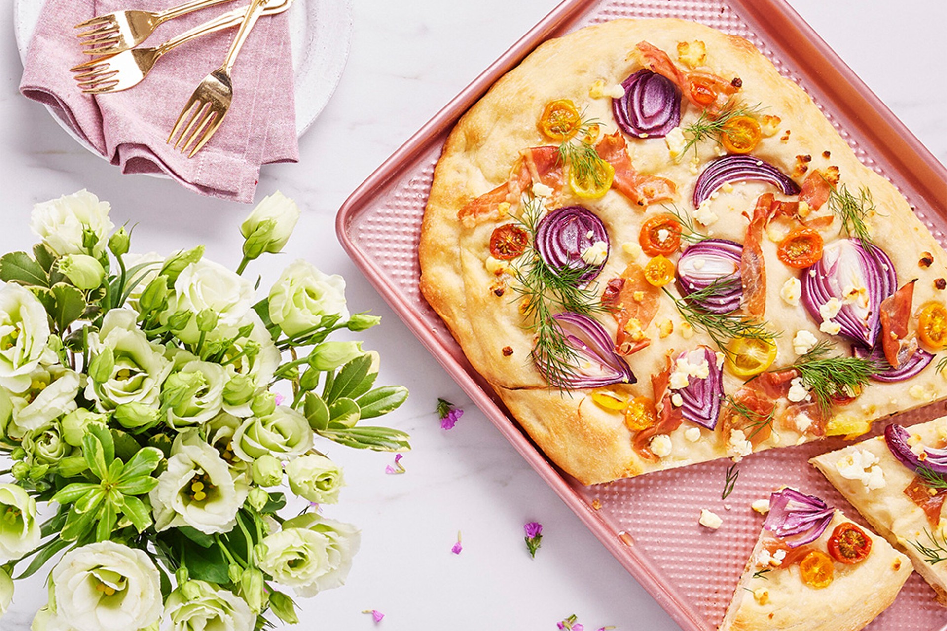 A veggie-packed focaccia sits on a pink sheet pan
