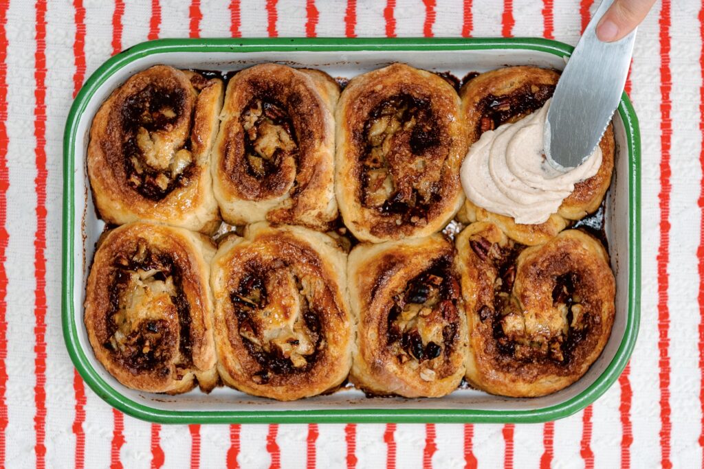 Tray of cinnamon apple buns with cream cheese frosting being applied