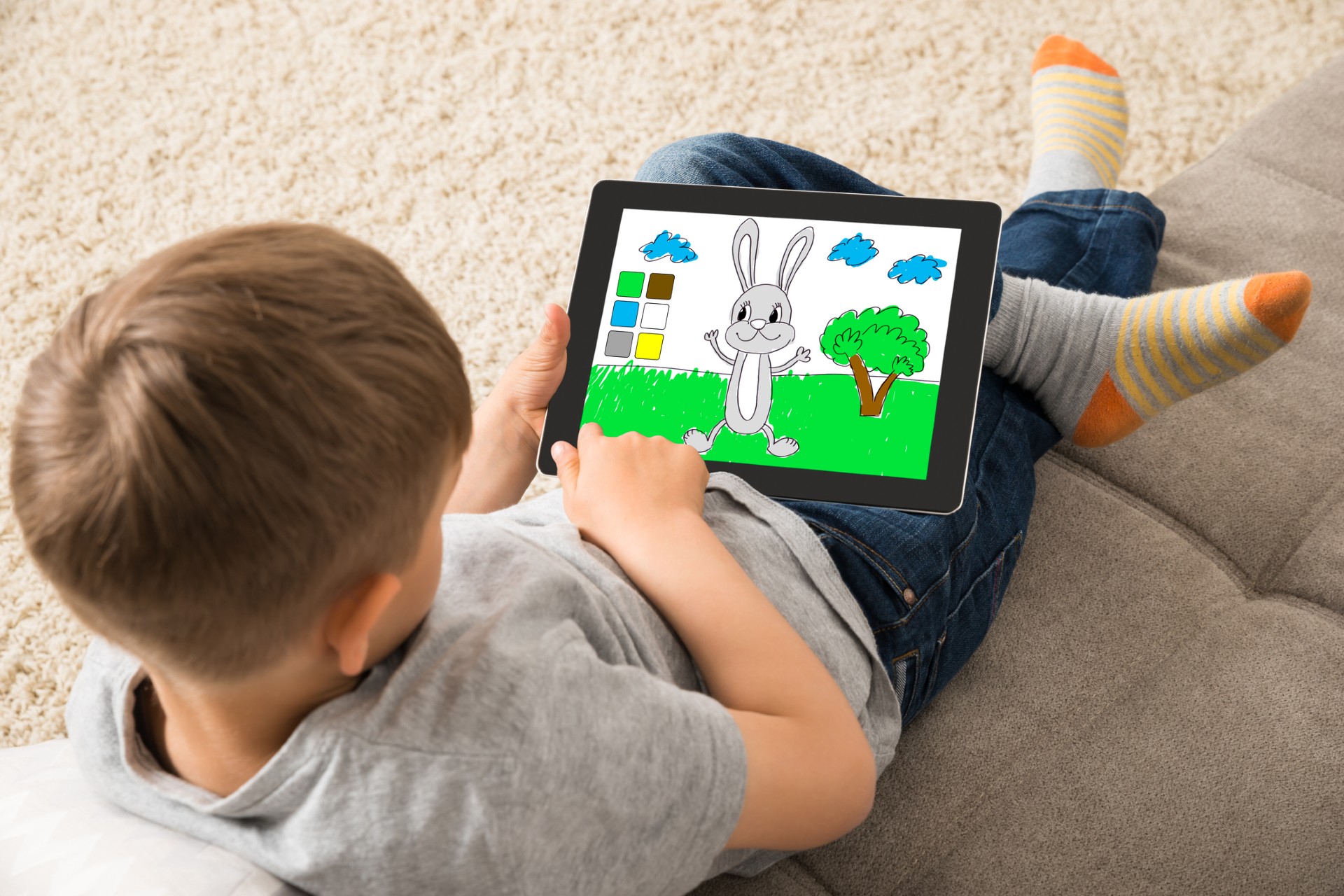 An overhead photo of a child looking down at a tablet screen that displays a drawing app