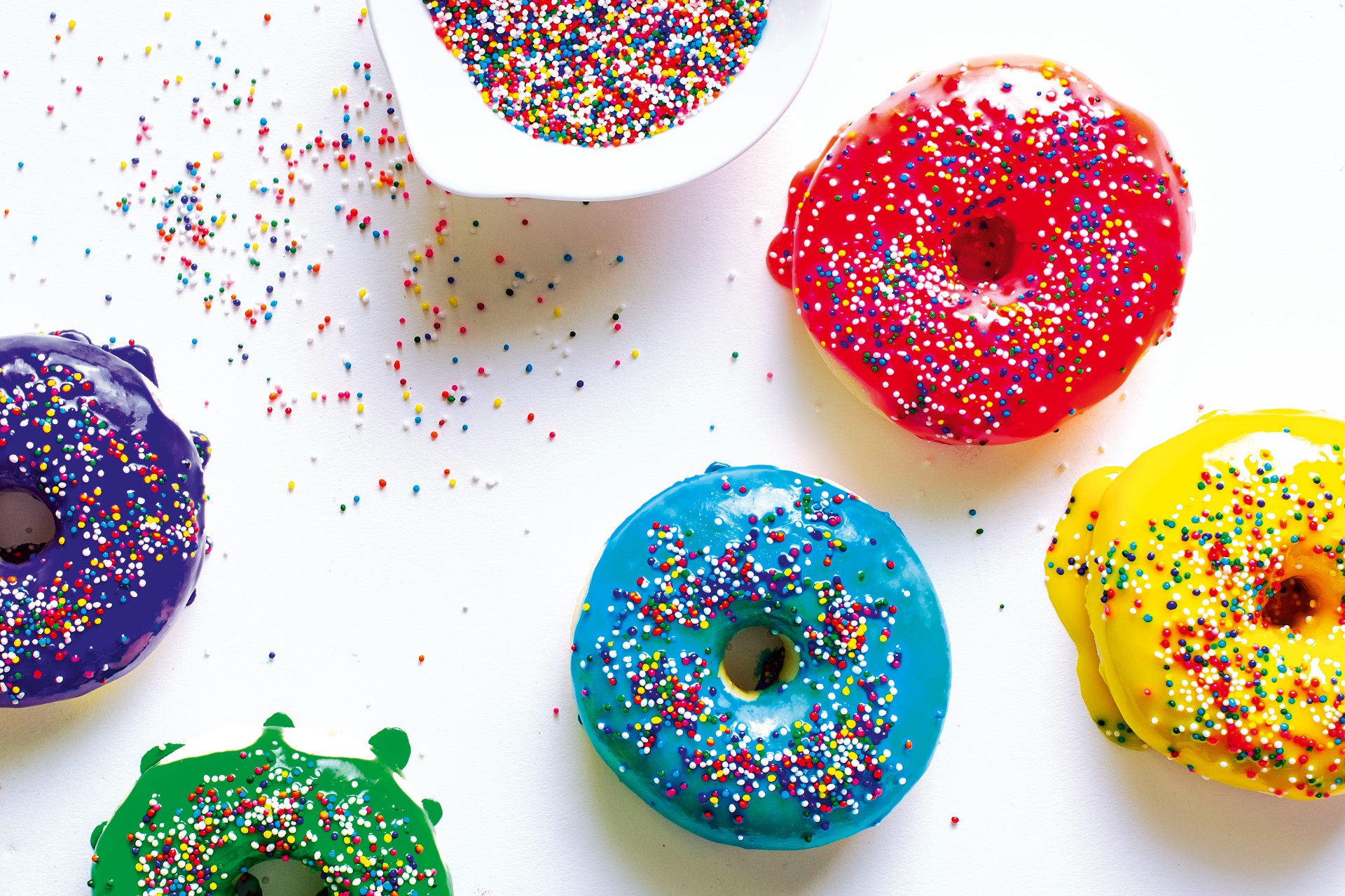 White surface with colourful iced and sprinkled doughnuts