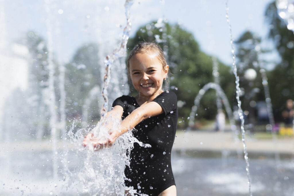 A young girl plays in a water fountain at a splash pad on a summer day.